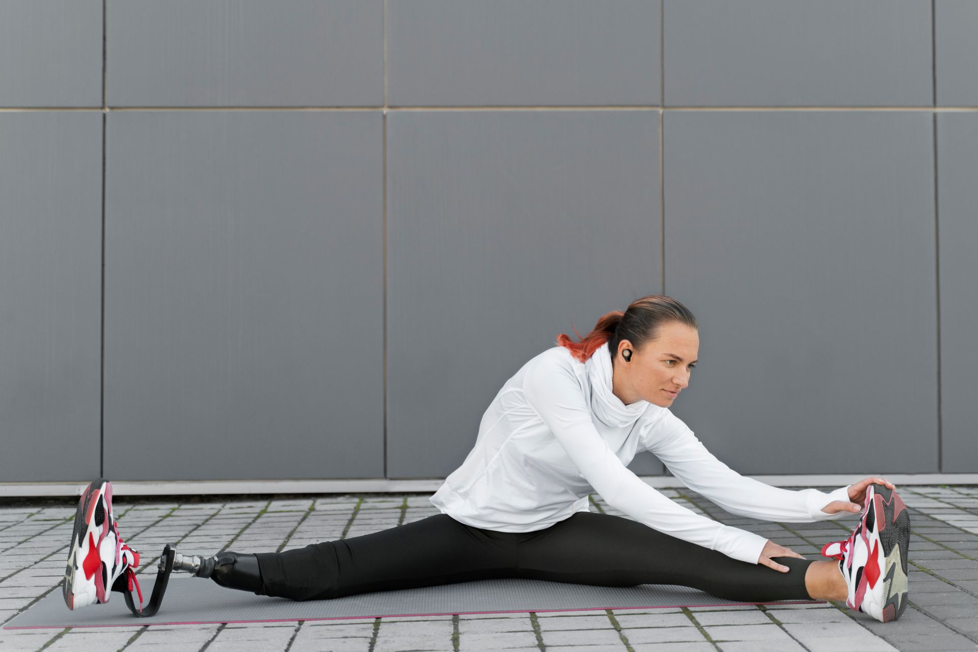 A woman with a prosthetic leg is stretching her legs on a mat.