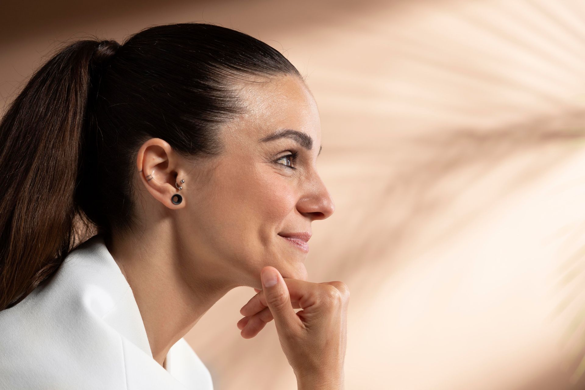 A woman with a ponytail is smiling and touching her face.