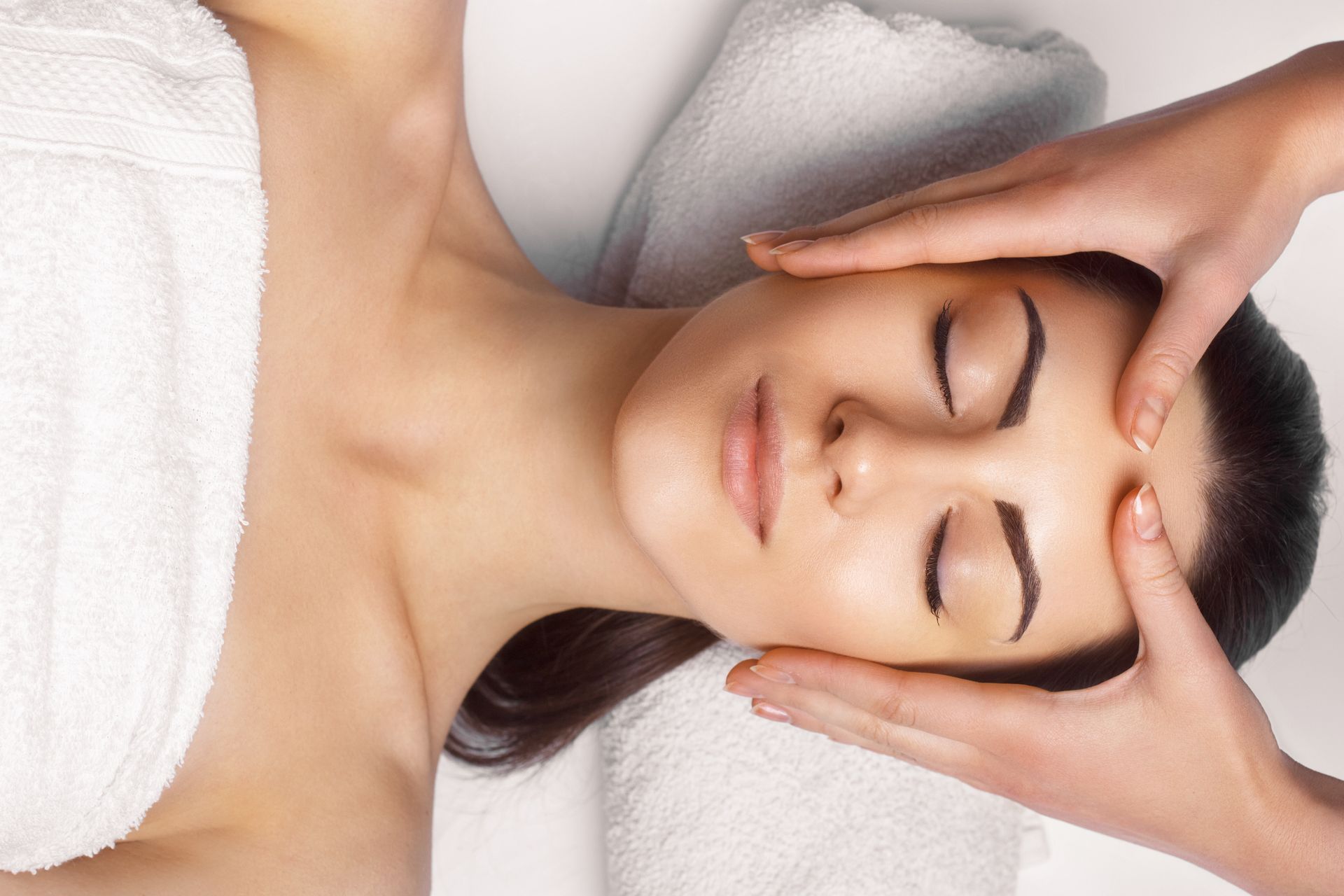 Person receiving a facial massage with eyes closed, hands gently touching the temples on a spa bed