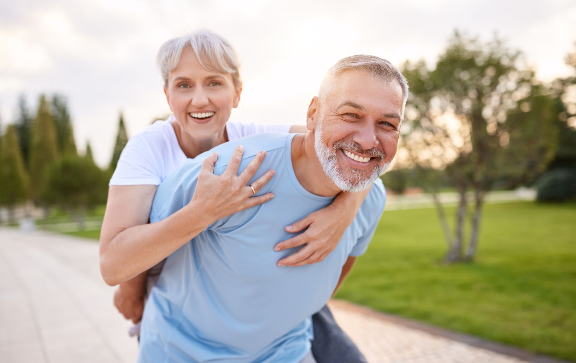 Elderly man giving woman piggyback ride outdoors, both smiling.