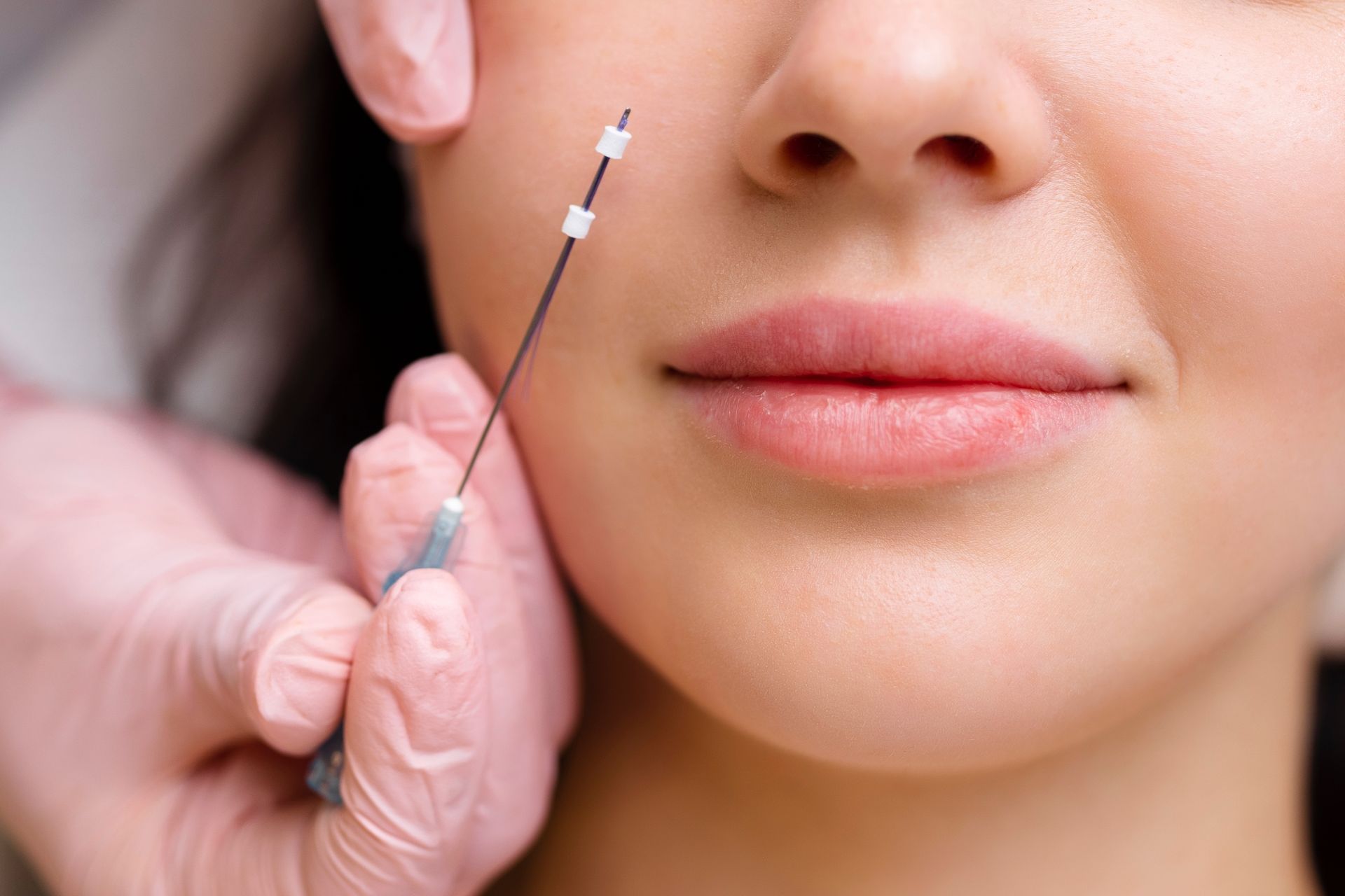 A hand holding a syringe near a woman’s cheek during a cosmetic injection procedure