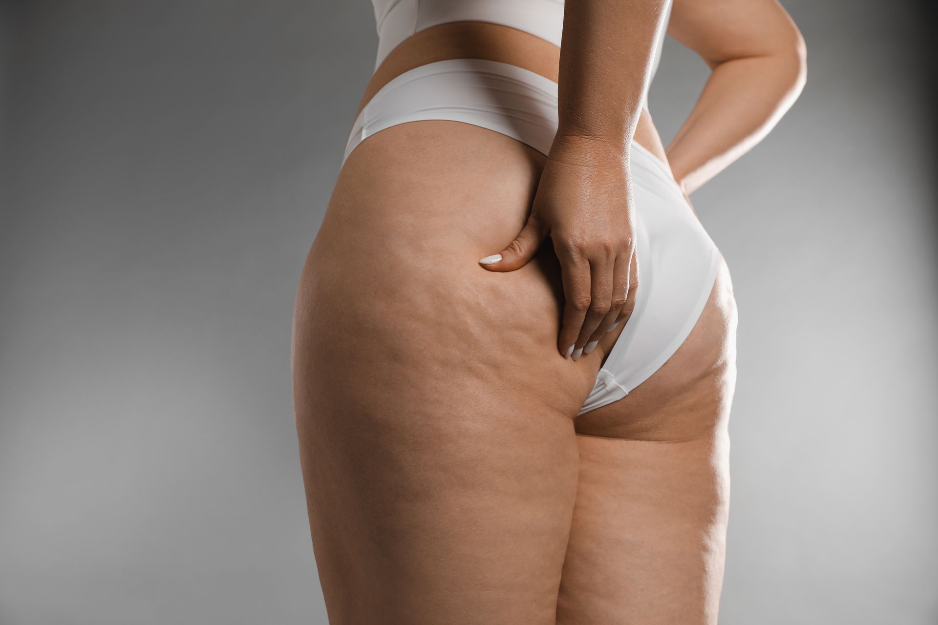 Back view of a person in white underwear, hand touching their hip against a gray background