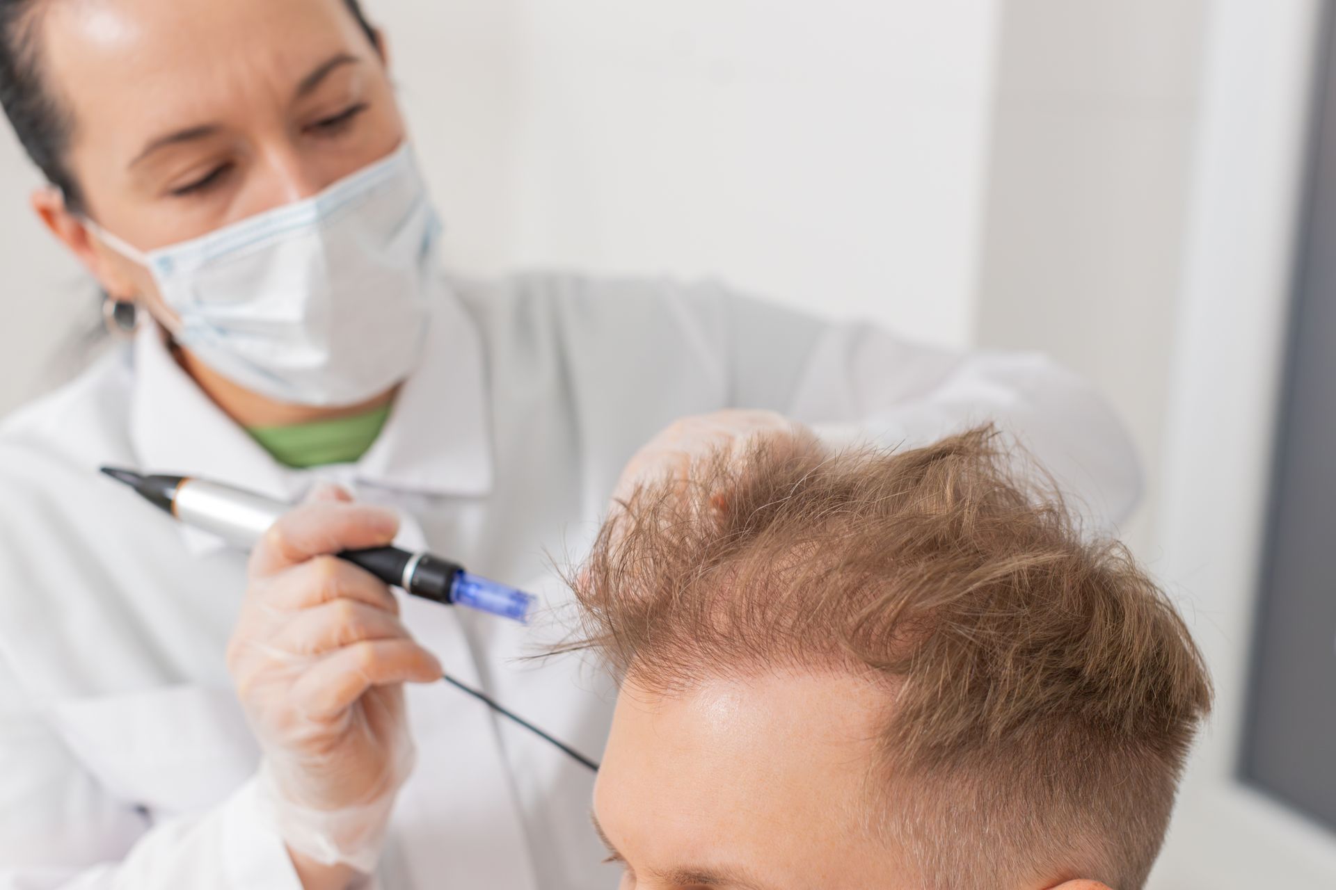 A woman in a mask is applying a needle to a man 's hair.