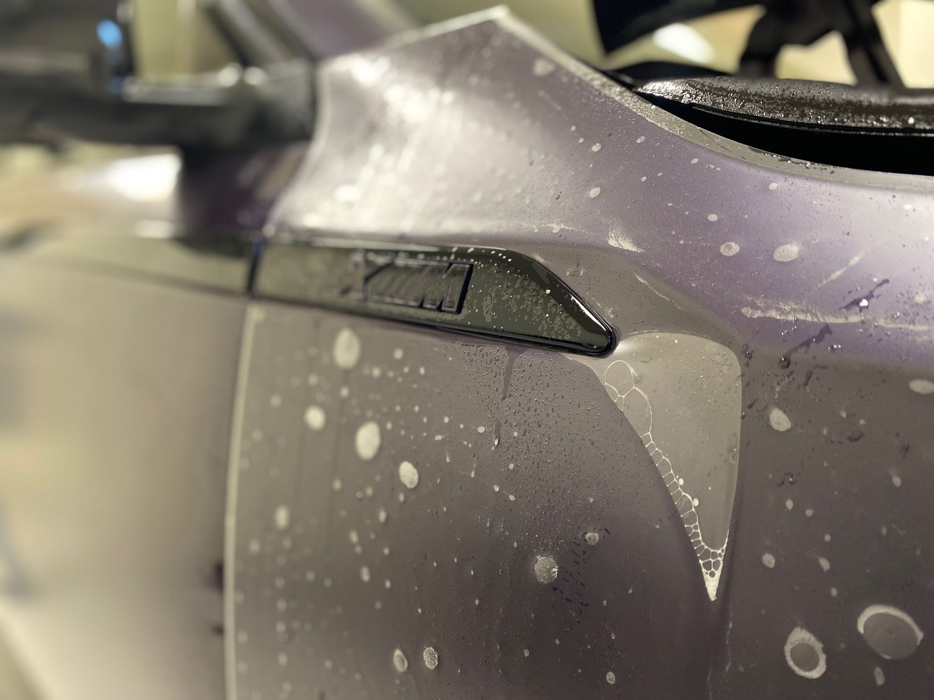 Close-up of a wet, purple car with black trim, showing water droplets and side marker light.