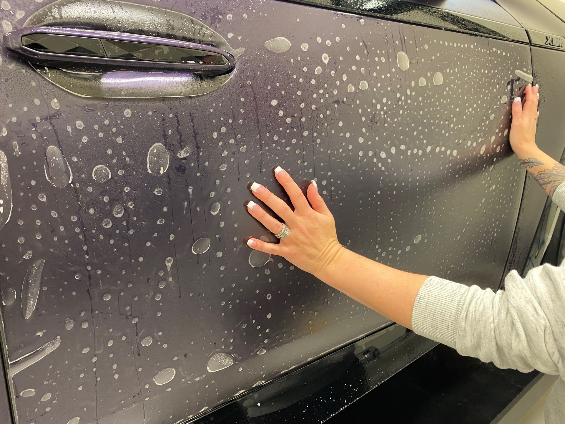 Person smoothing protective film on a black car door with soapy water visible.