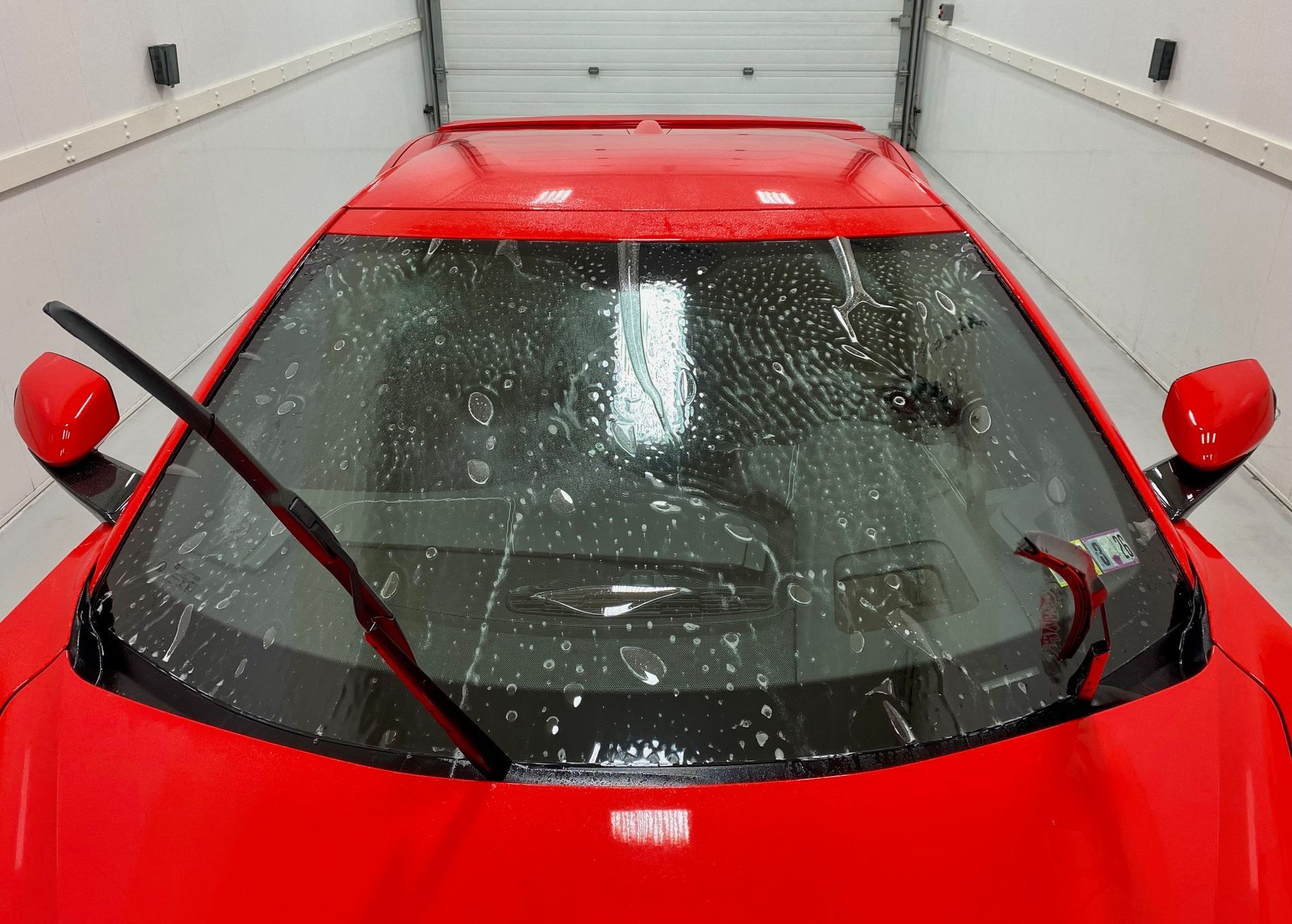 Red sports car with windshield wipers cleaning the glass, wet with water.