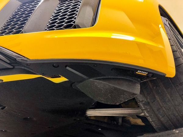 Yellow car's front undercarriage, showing a black splitter and tire.