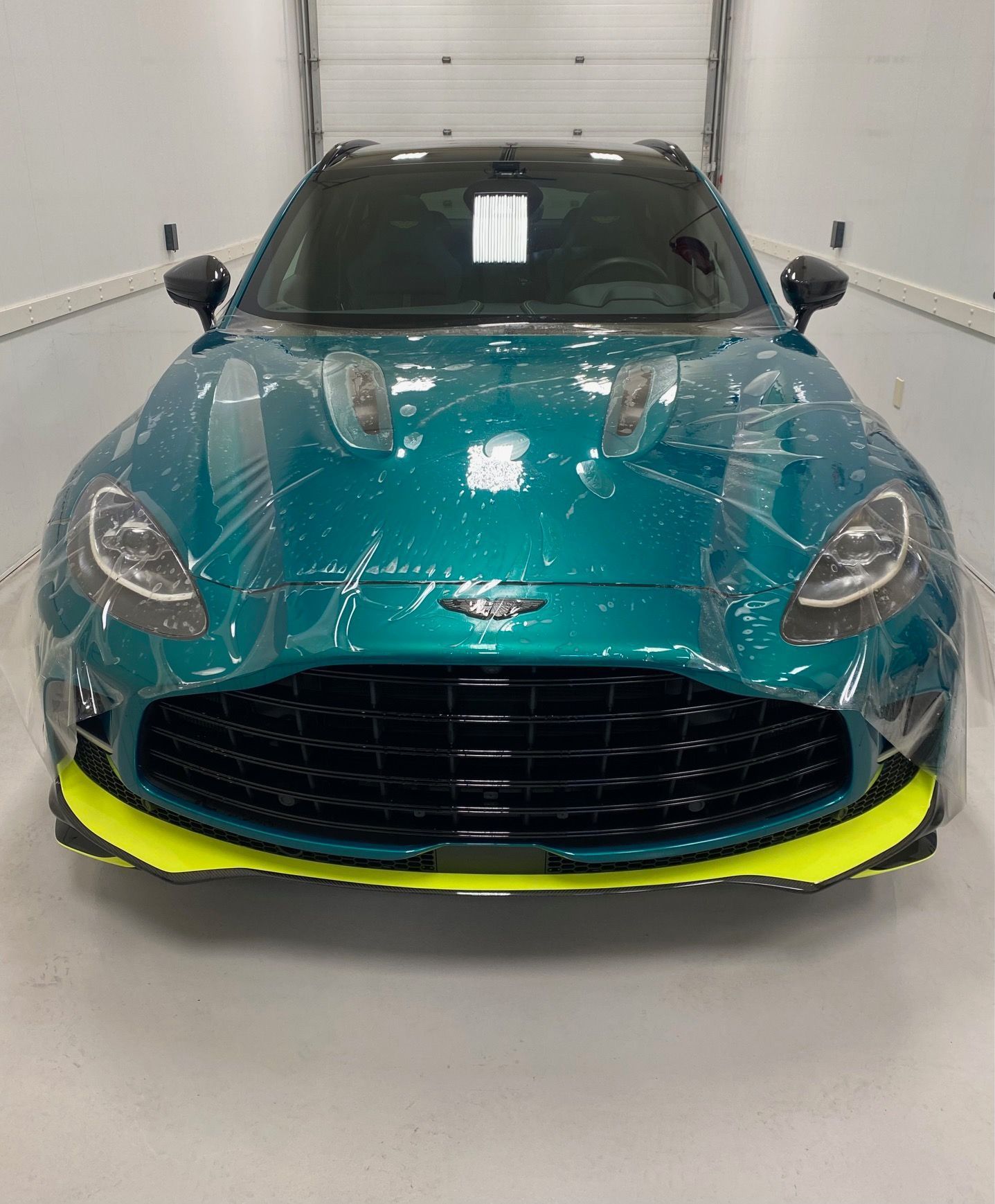 Green Aston Martin DBX SUV with yellow accents in a garage.