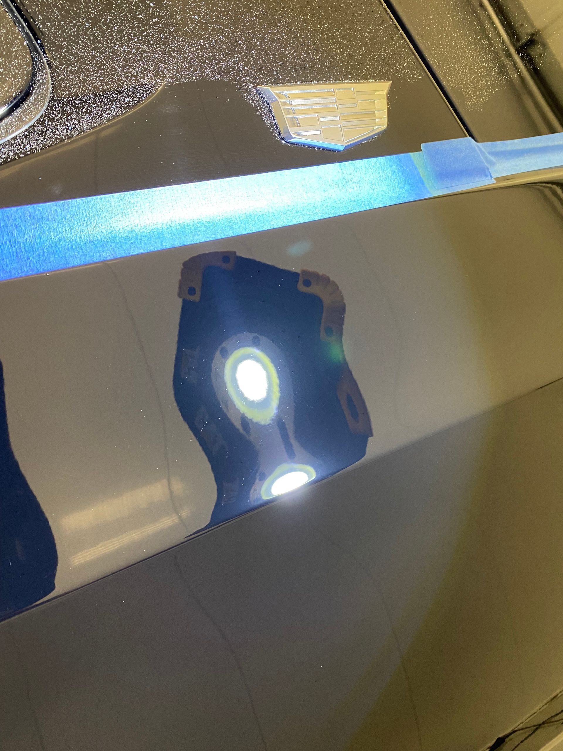 Reflections on a dark car hood showing distorted shapes, with a long blue light across the top.