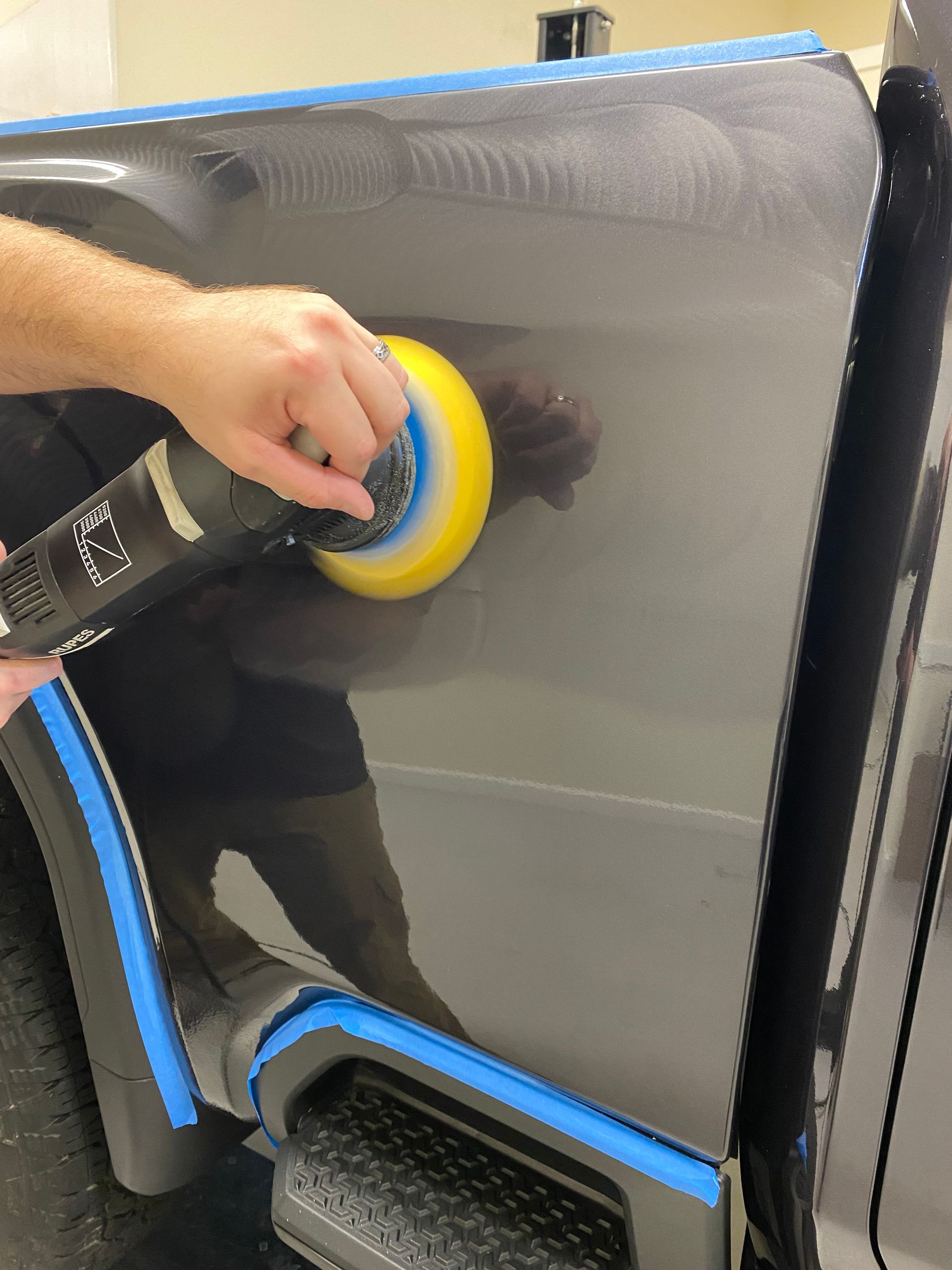 Person using an orbital polisher to buff a black vehicle panel.