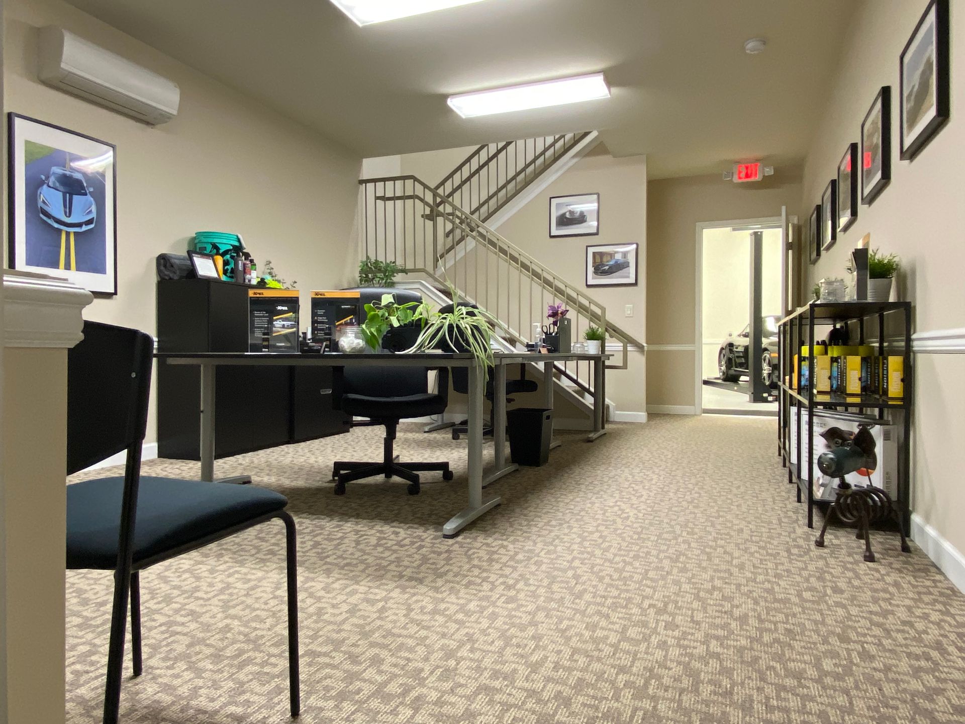 Office hallway with desks, chairs, stairs, and framed pictures on the walls