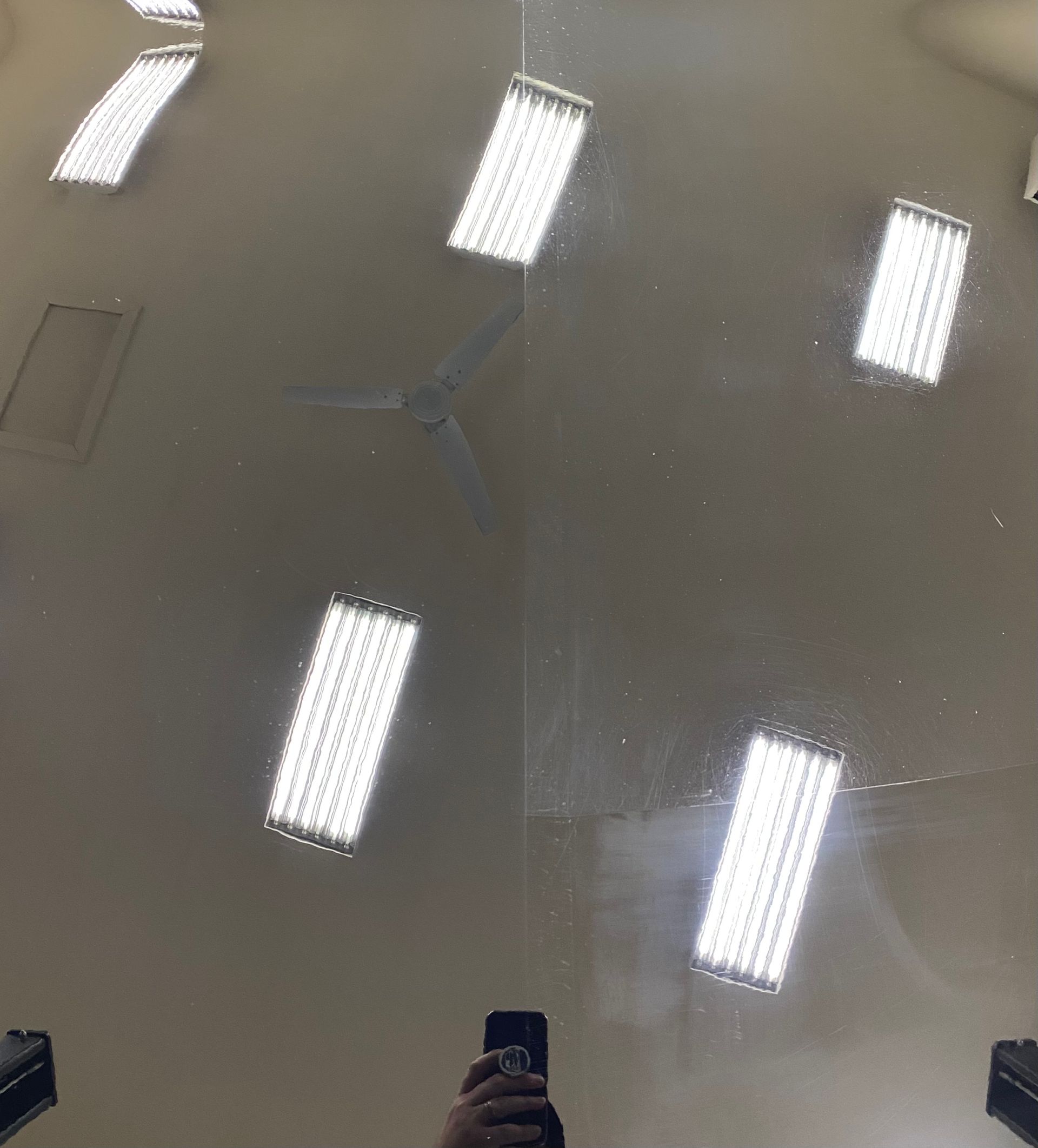 Reflections of six bright rectangular ceiling lights on a shiny, light-colored floor; hand holding a phone in view.