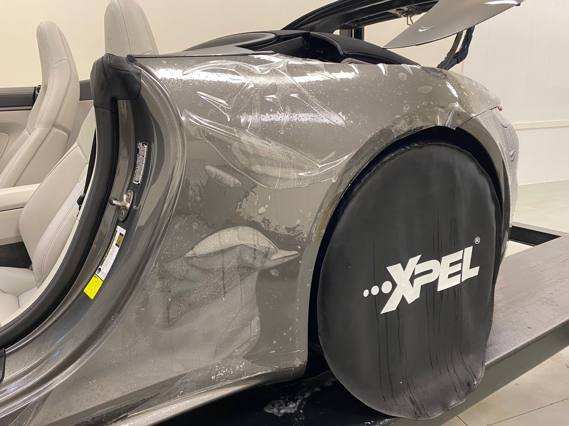 Gray sports car being worked on with protective coverings, the Xpel logo is visible.