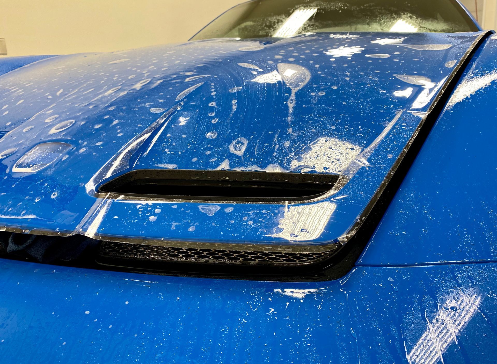 Blue car hood with open air vent, covered in soapy water.