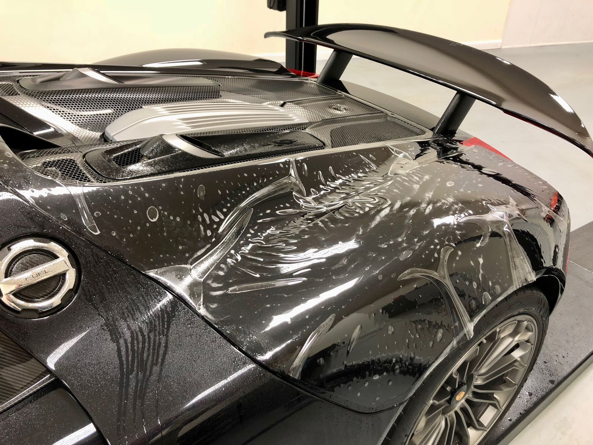 Black sports car with wet soapy detailing on the rear quarter panel and spoiler.