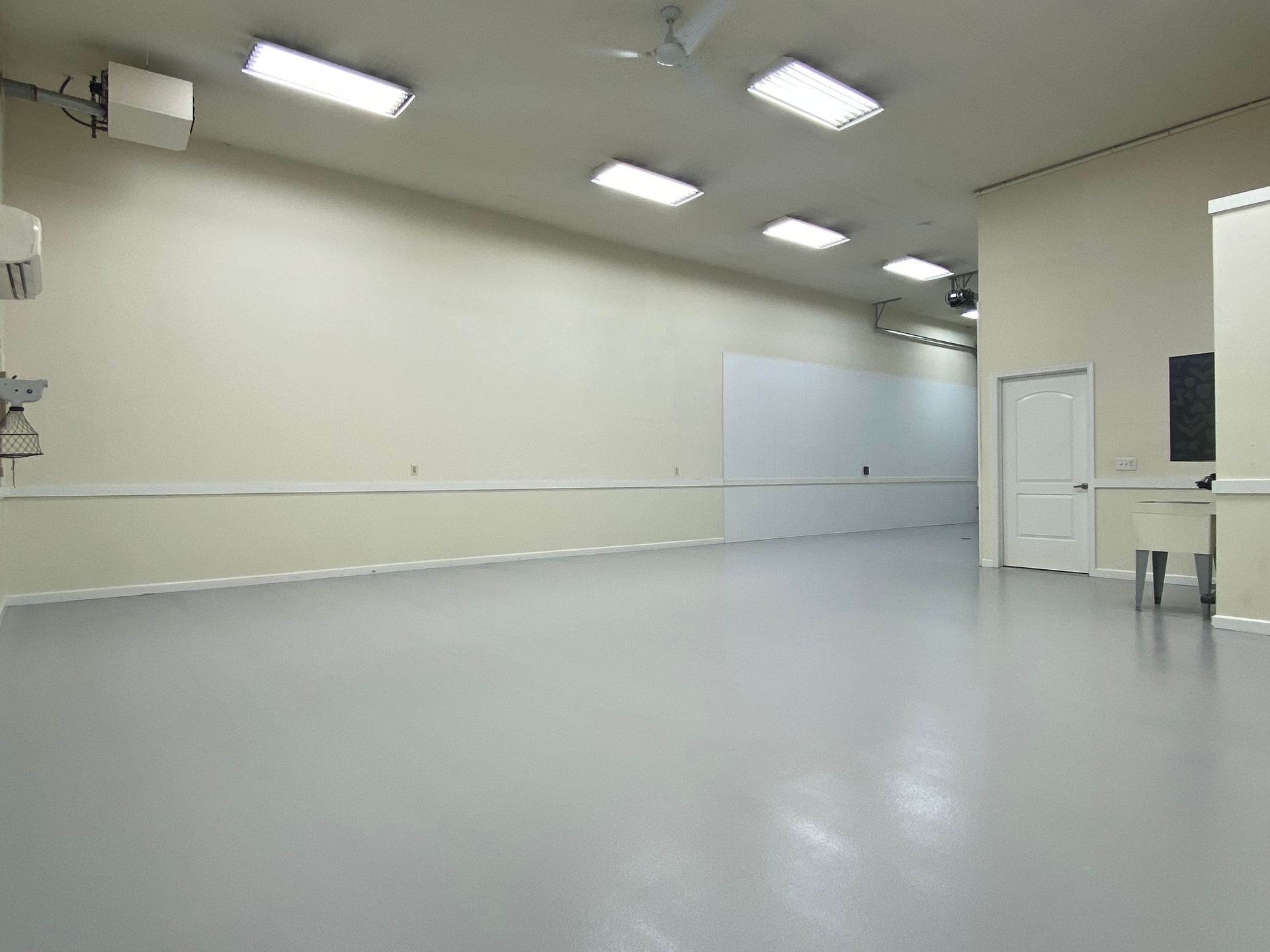Empty indoor studio with pale walls, gray floor, and overhead fluorescent lights