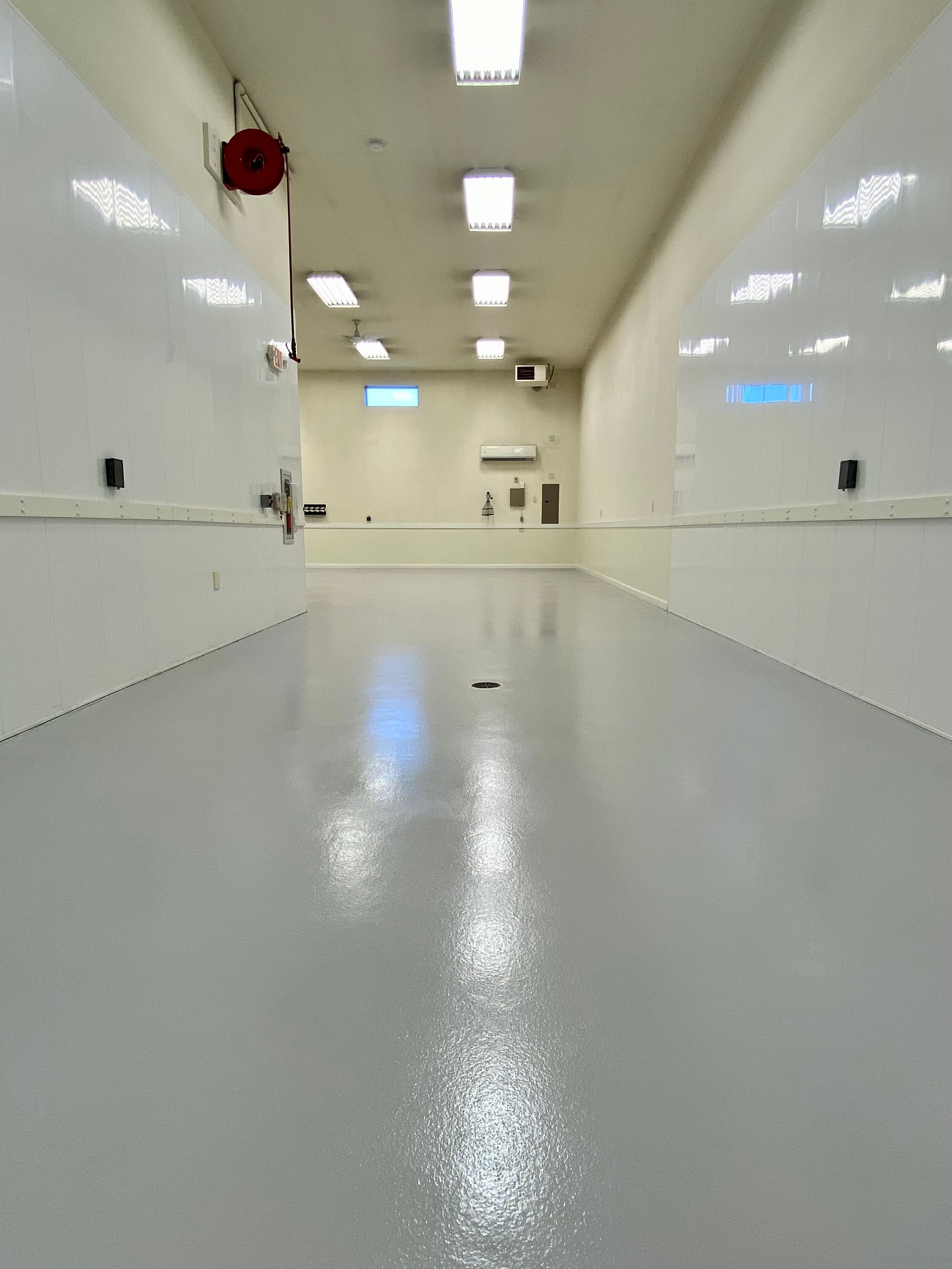 Empty white industrial hallway with glossy gray floor and overhead lights