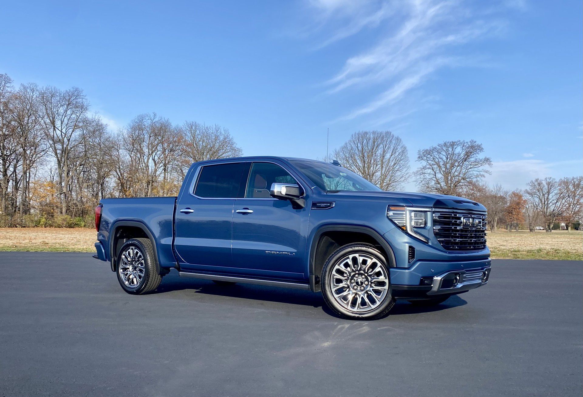 Blue GMC Sierra truck parked on pavement against a sunny sky.
