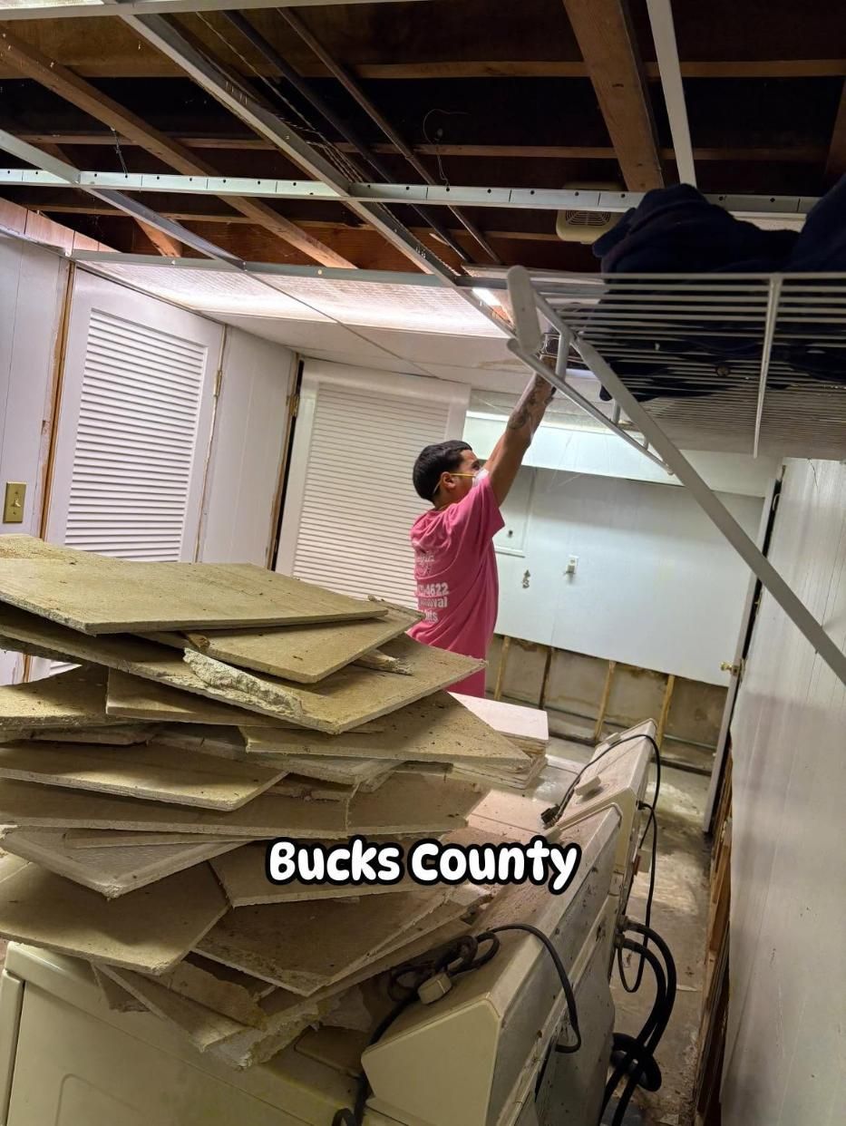 Person in pink shirt working amid collapsed ceiling debris in a room with exposed beams and cabinets
