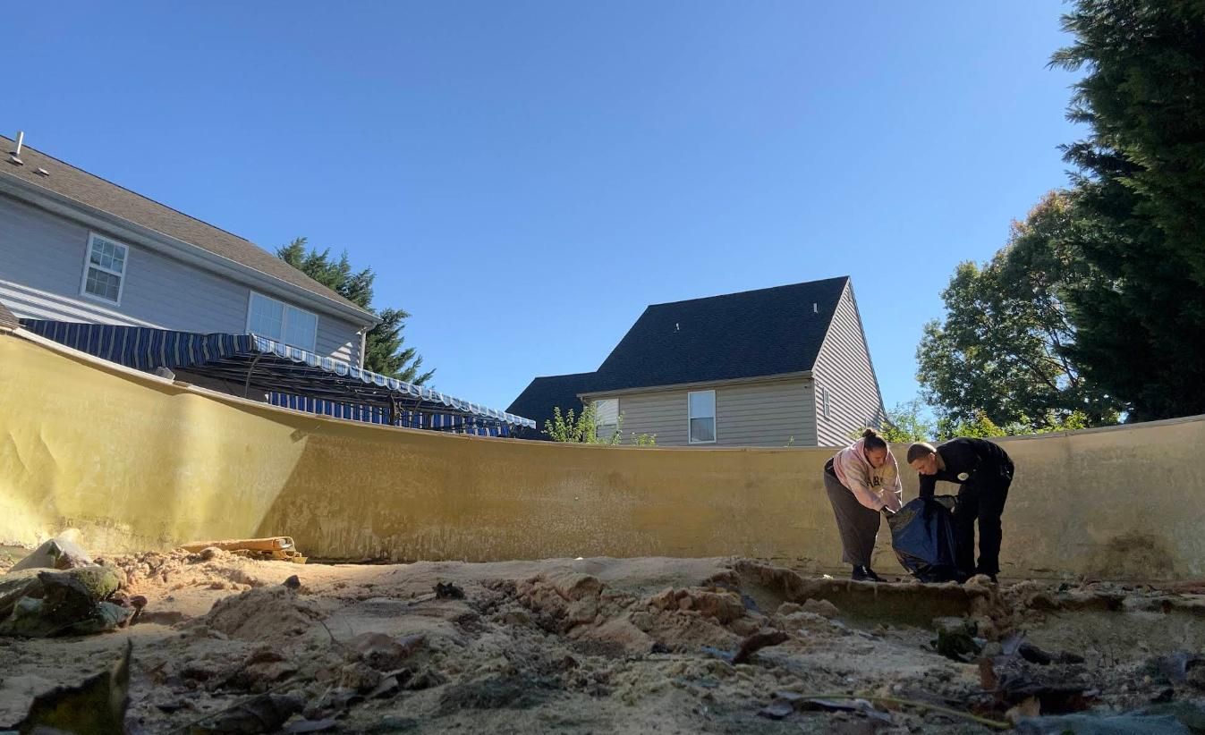Three people working in a drained pool. Light brown walls and dirt on the bottom.