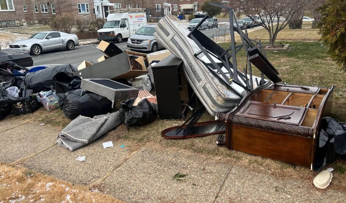 Discarded furniture and trash piled on a curb in a residential area.