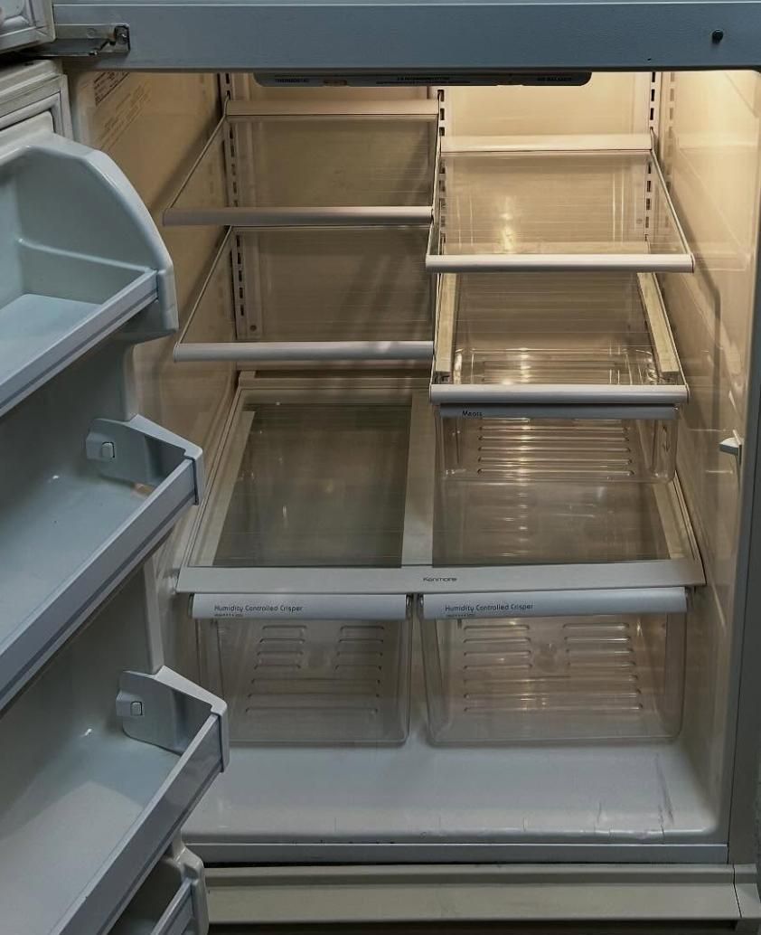 Empty refrigerator with clear shelves and bins, door ajar, interior lit.