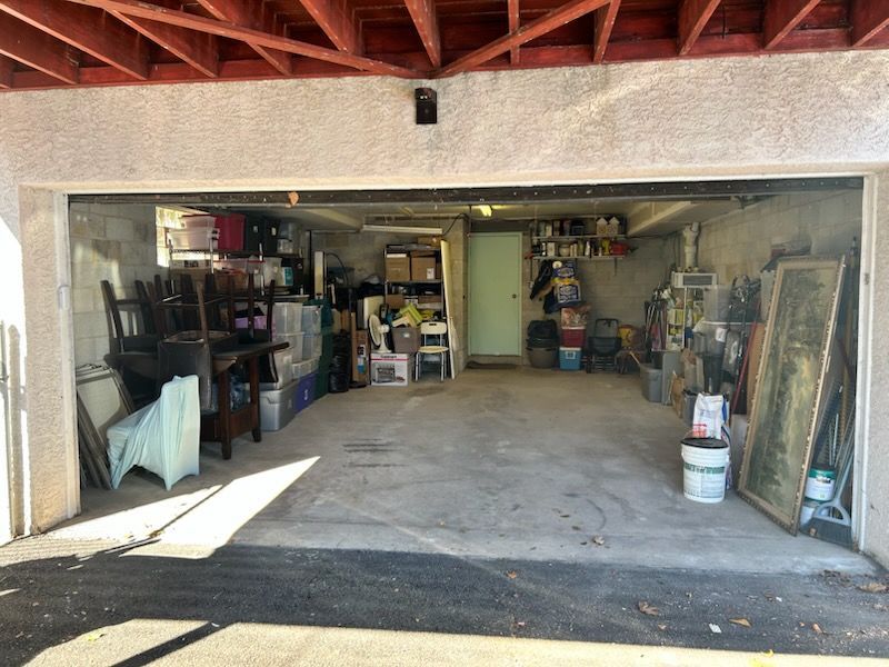 Open garage workshop with shelves, tools, bins, and stored items under a red wood-beam ceiling.
