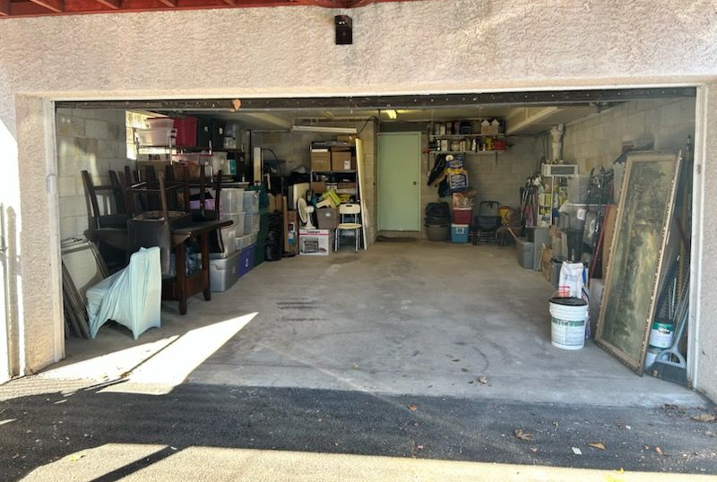 Open garage with stored household items, shelves, and tools in dim light.