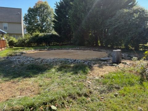 Backyard with a large gravel patio area, trees, and a house in the background