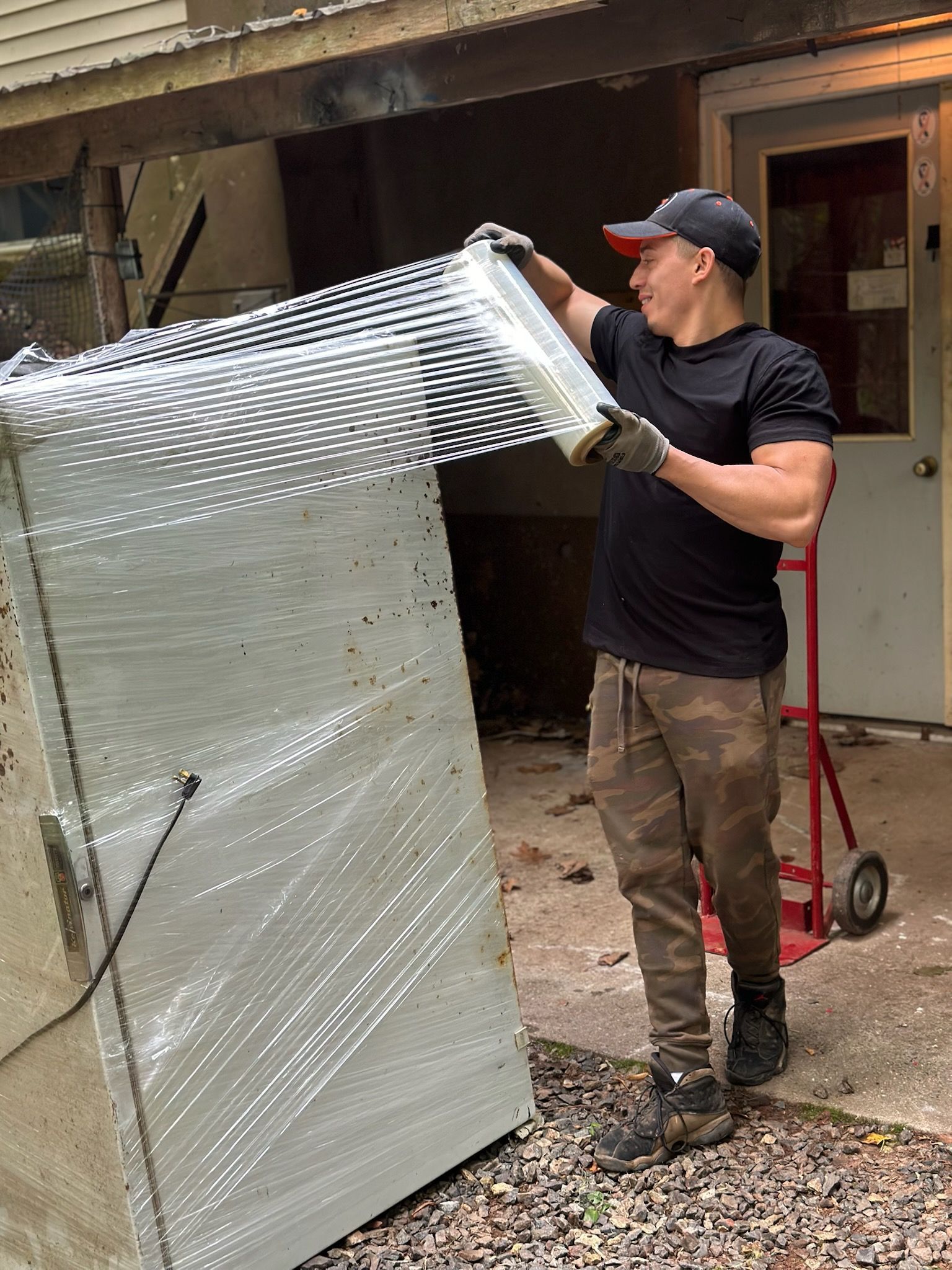 Worker wrapping a large white panel in clear plastic outside a building
