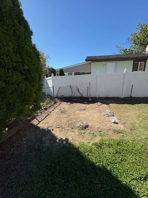 Backyard with dry patchy grass, white fence, and a house under a clear blue sky