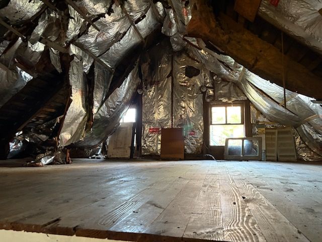 Empty attic room with exposed rafters, shiny insulation, windows, and a wooden floor