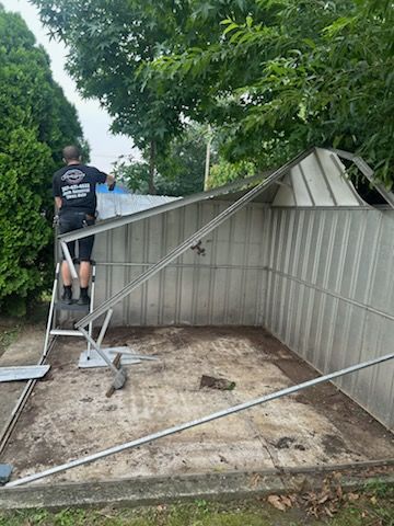 Person working to straighten a bent metal shed roof in a yard