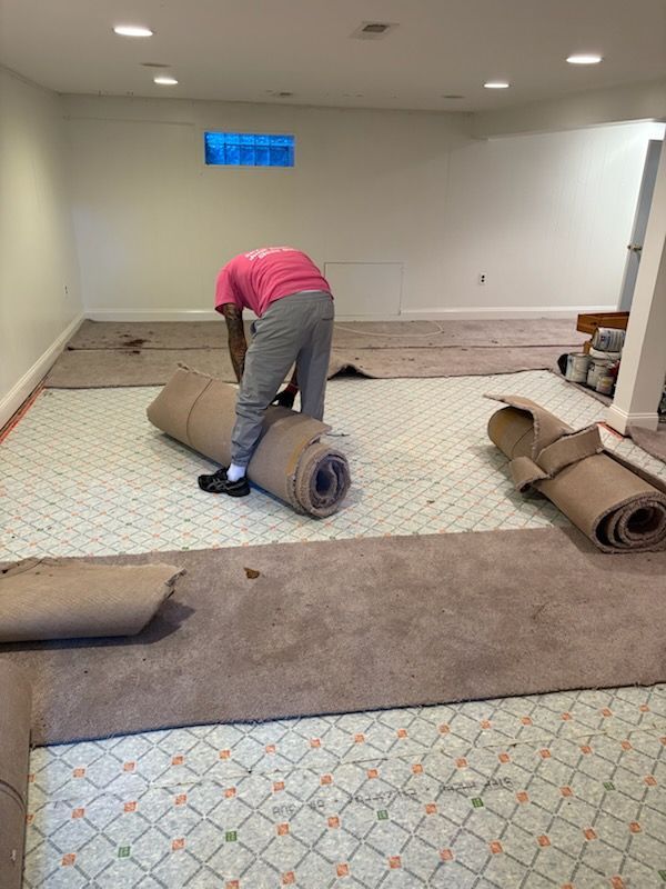 Person rolling up carpet in an empty room with carpet tiles, preparing the floor for installation