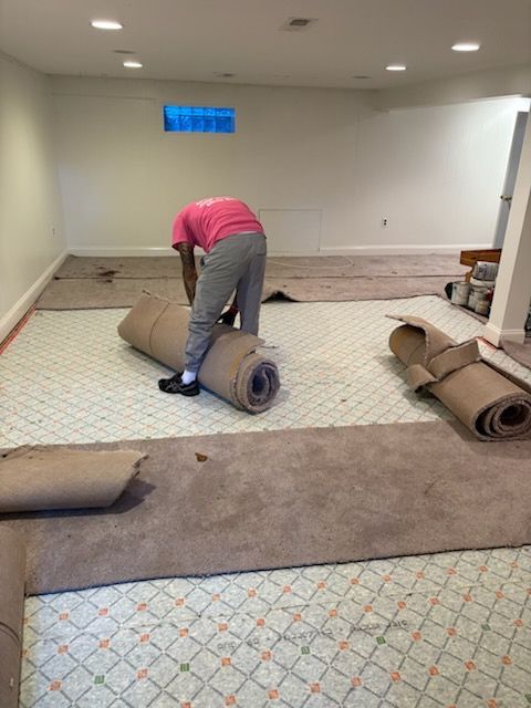 Person rolling carpet in an empty room with patterned flooring and several carpet rolls nearby
