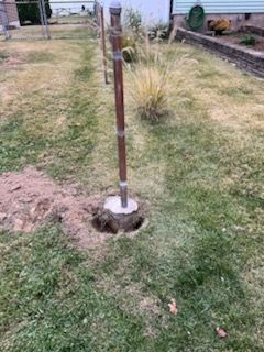 Rusty metal post set in a concrete base with a hole in the ground beside it in a grassy yard