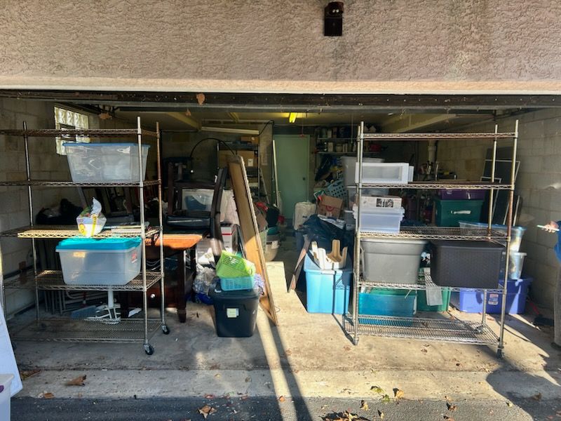 Campsite kitchen setup under a garage-like overhang with tables, coolers, and cooking gear in shade