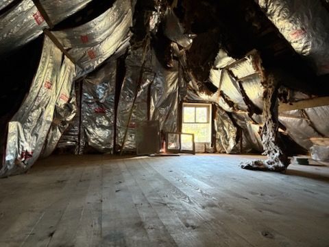 Small empty room with a wooden floor and walls lined with shiny black insulation around a window.