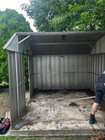 Partially assembled metal shed frame on a concrete slab, with a person working at the right edge.