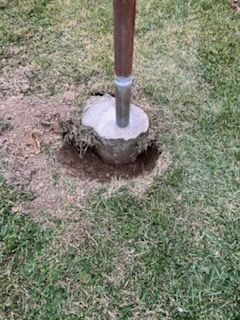 Wooden post set in a concrete footing with exposed soil hole in a grassy yard