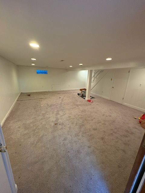 Empty basement room with carpet, recessed lights, white walls, and a blue TV on the far wall