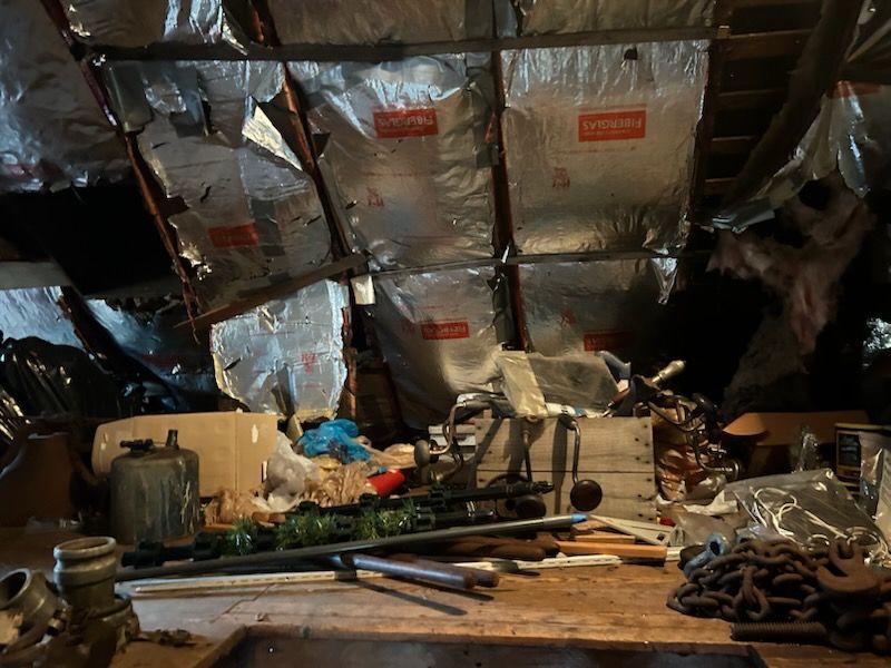 Dim attic workshop with foil-insulated ceiling and scattered tools on a cluttered workbench.