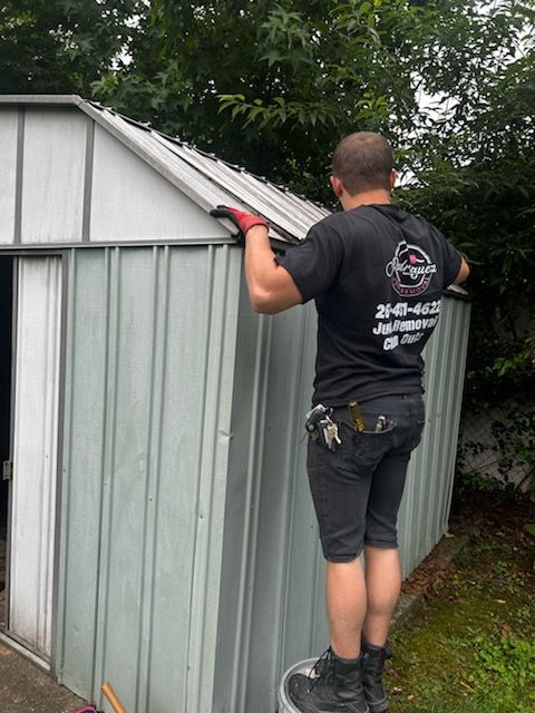 Man standing on a small metal shed roof, inspecting the roof edge with gloved hands