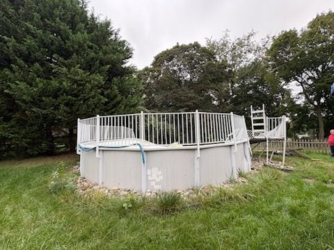 Above-ground pool with white railing in a grassy backyard, surrounded by trees