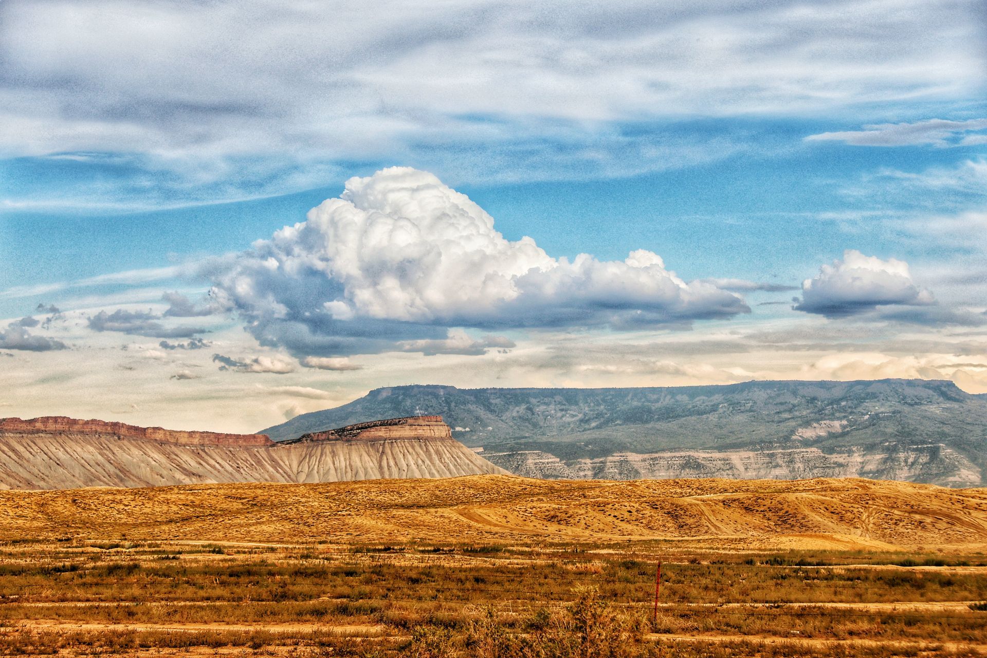 A large cloud is floating over a desert landscape with mountains in the background.