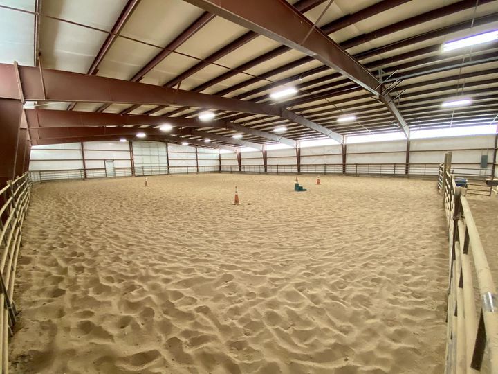 A large indoor arena filled with sand and a fence.