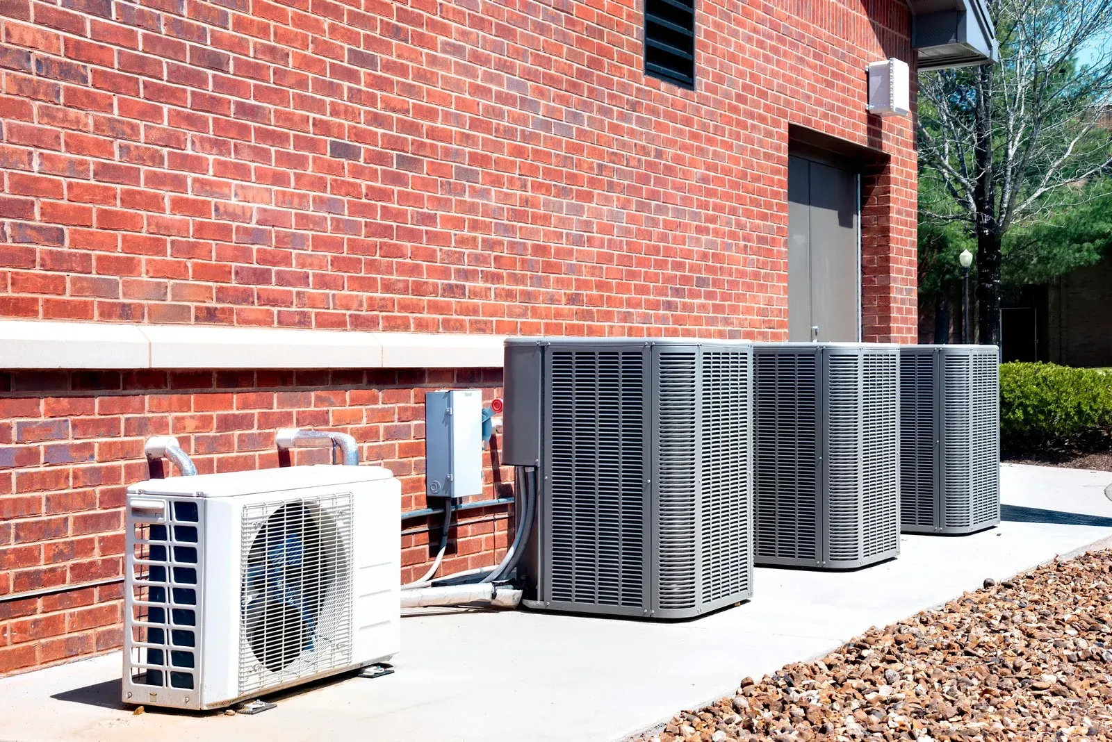 Air conditioning units lined up against a brick building exterior.