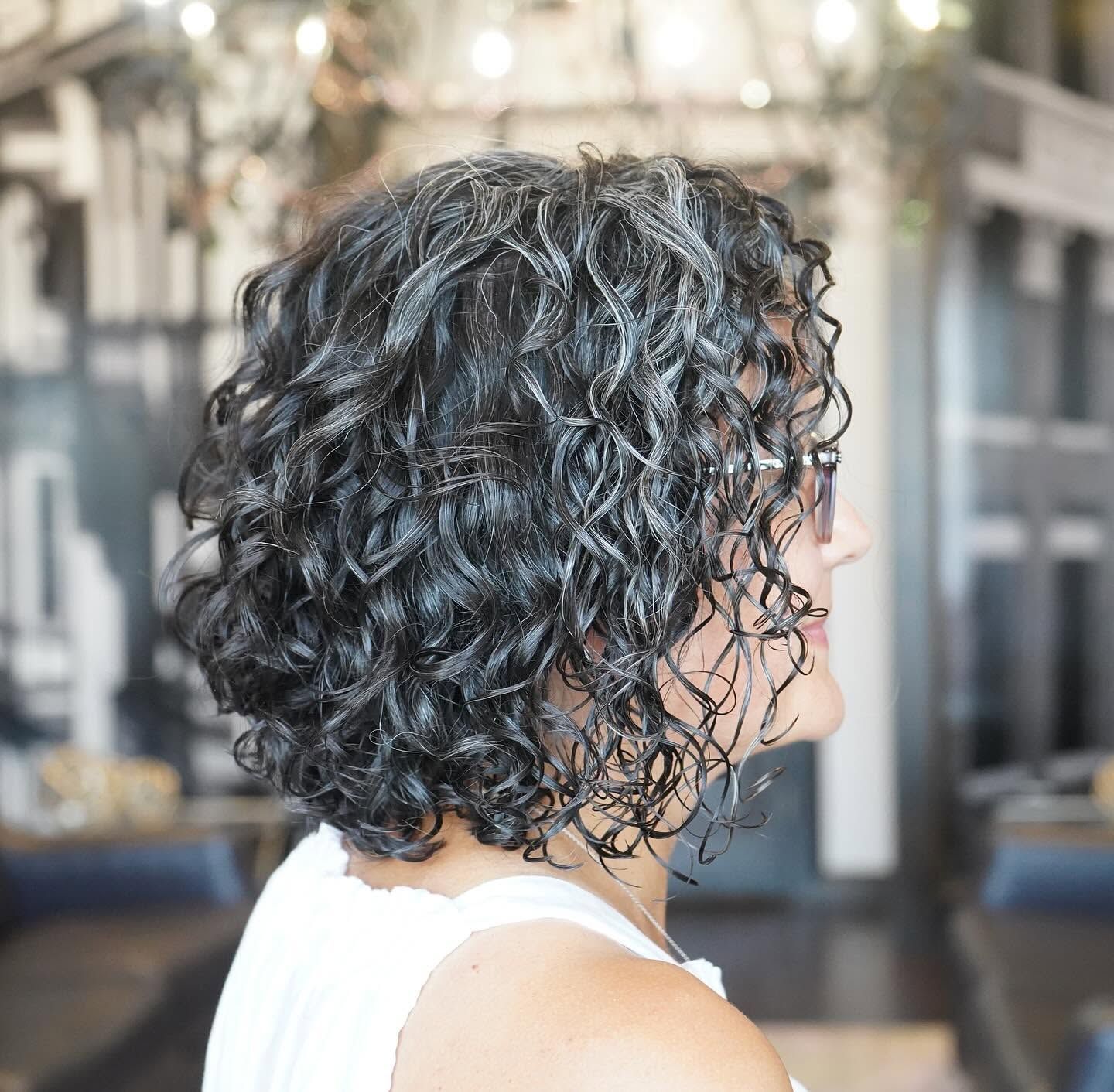 Side profile of a person with short curly dark hair in a bright salon setting