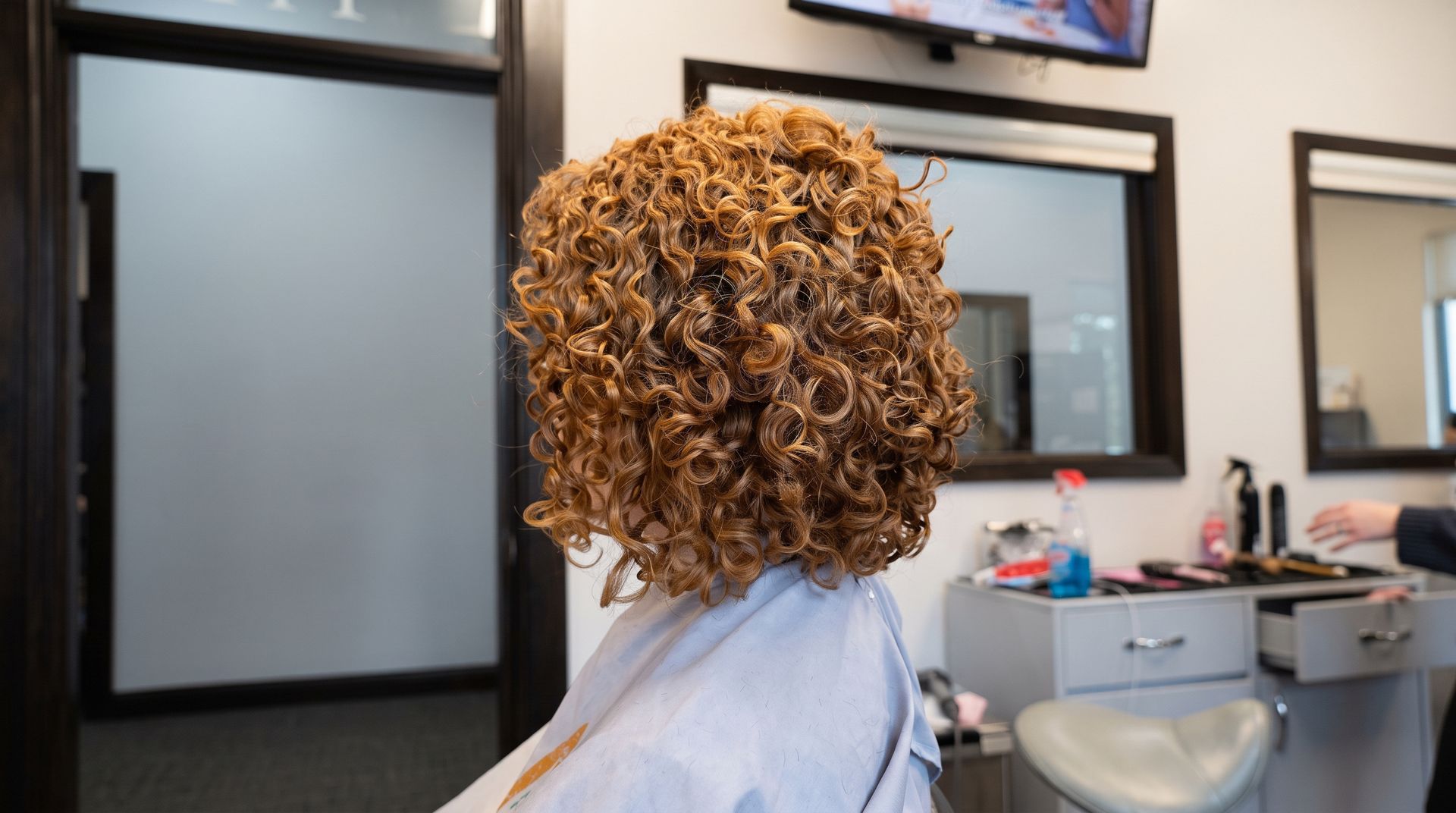 Woman styling a seated client’s curly hair in a salon, both smiling