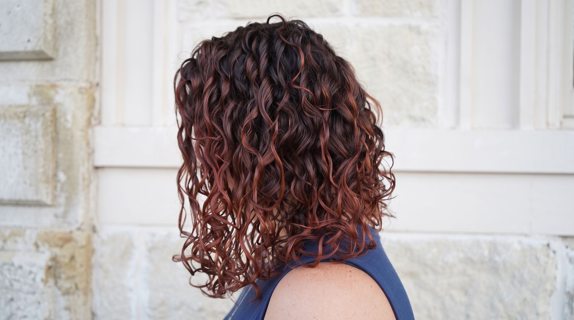 Woman with long dark hair and bright magenta highlights in a salon chair, side profile.